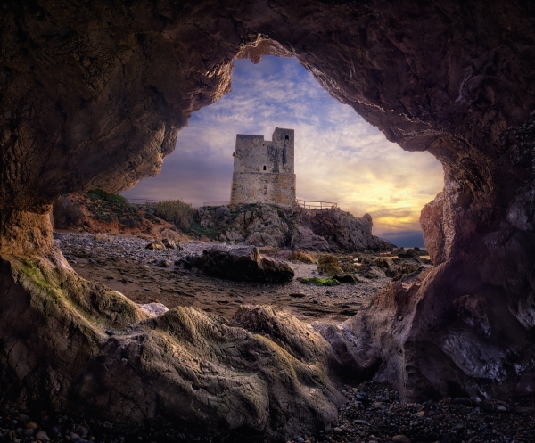 Vista majestuosa del atardecer de una torre de vigilancia costera a través de la apertura de una cueva marina.