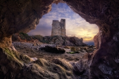 Vista majestuosa del atardecer de una torre de vigilancia costera a través de la apertura de una cueva marina.